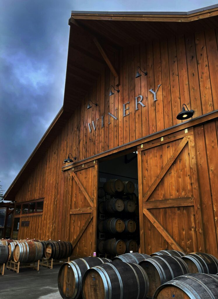 pexels photo 34069061 34069061 A rustic wooden winery barn with wine barrels stacked outside on a cloudy day.