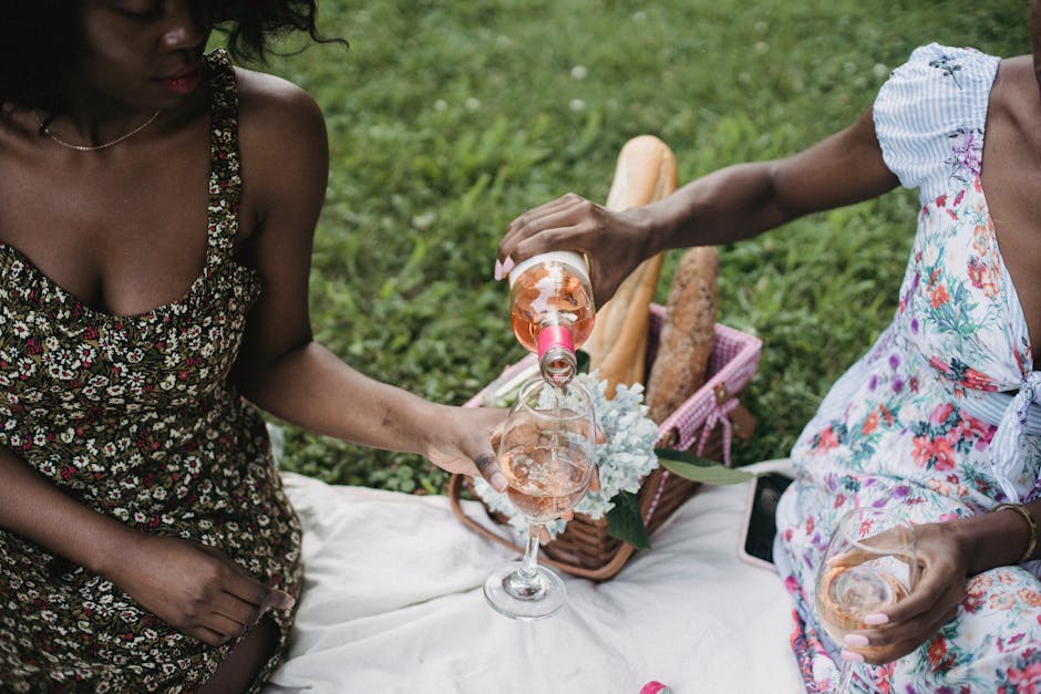 pexels photo 5050172 5050172 Two women enjoying a picnic with wine in a sunny park setting, capturing summer leisure.