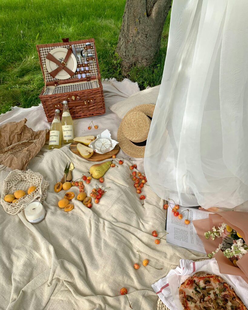 Charming outdoor picnic with fruits, wine, and a wicker basket under a tree.